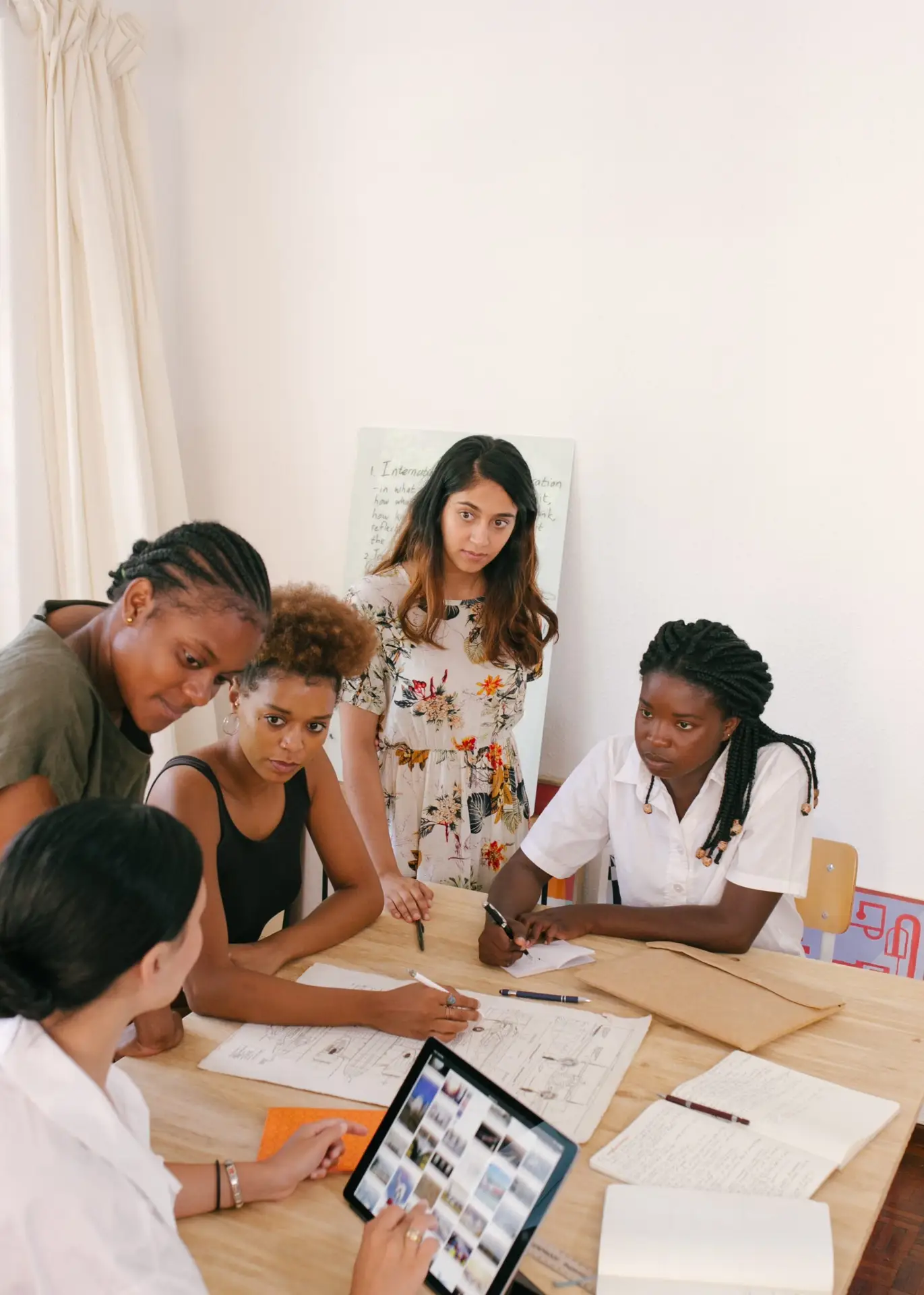 Group of diverse individuals collaborating around a table, reviewing documents and using a tablet, emphasizing teamwork and communication in a professional setting.
