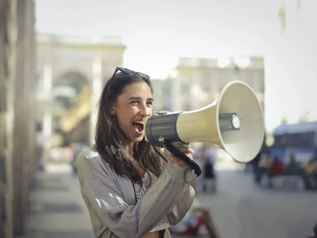 Woman enthusiastically using a megaphone outdoors, representing engagement and communication in digital marketing strategies.